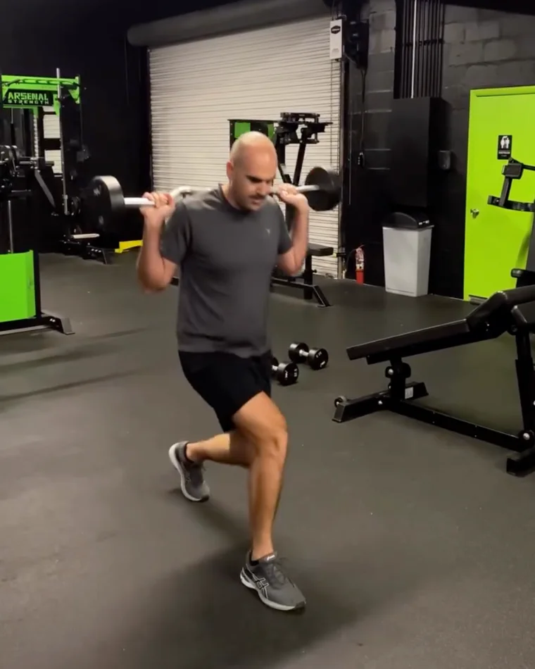 Jake mid forward lunge with a barbell across his shoulders, on the training floor