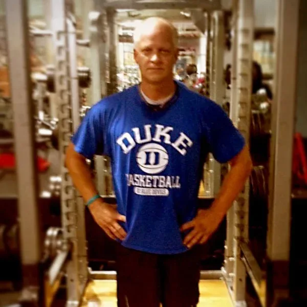 Karl standing between the uprights of a squat rack on the gym floor, hands on his hips